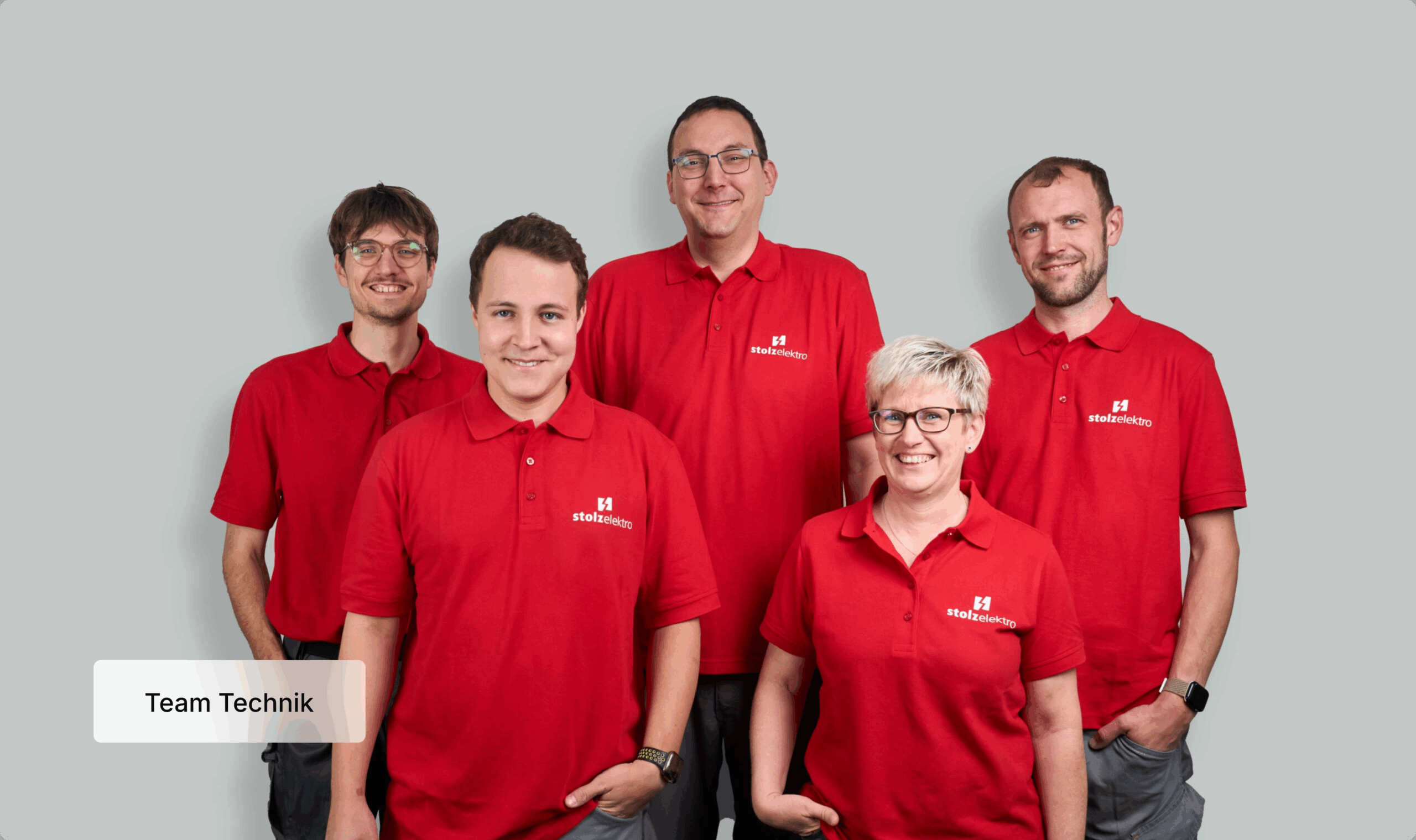 Fünf Personen in passenden roten Poloshirts mit Logos stehen lächelnd vor einem hellgrauen Hintergrund. In der Ecke steht die Aufschrift Team Technik.